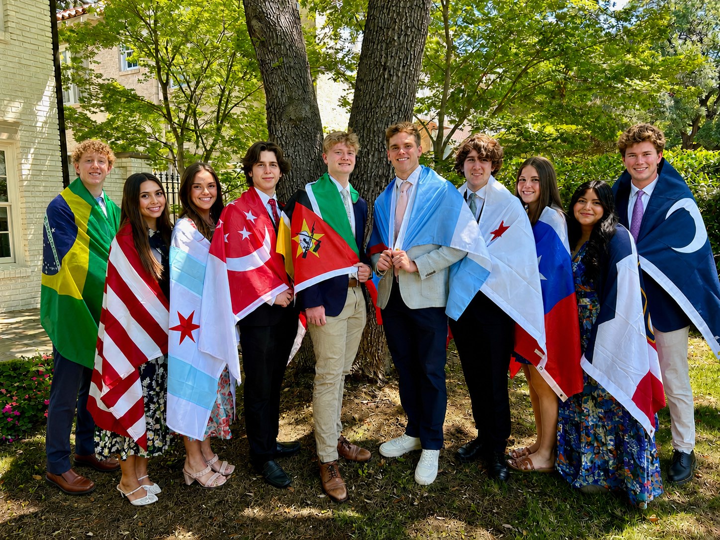 Ten Highland Park High School graduates standing under a tree, each wearing the flag of the place they will serve a mission